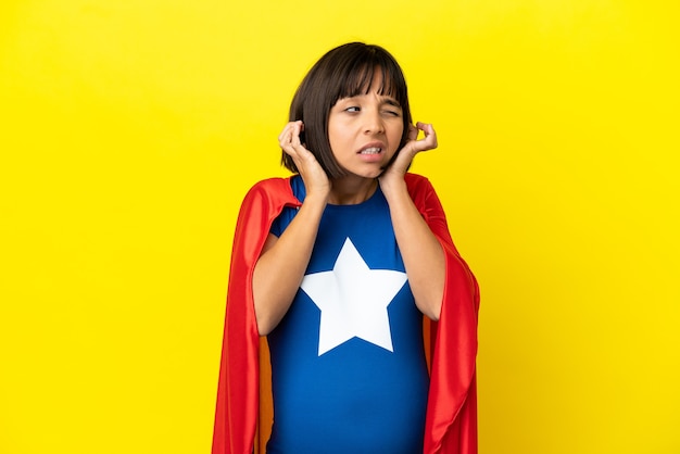 Superheld zwangere vrouw geïsoleerd op gele muur gefrustreerd en oren bedekt