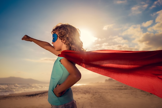 Superheldenkind op het strand Superheldenkind dat plezier heeft buiten Zomervakantieconcept