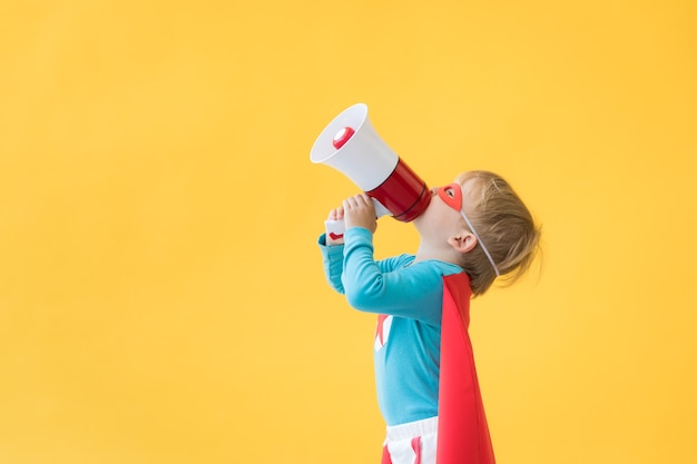 Superhero child against yellow paper background. Super hero kid wearing red mask and cape. Childhood dream and imagination concept