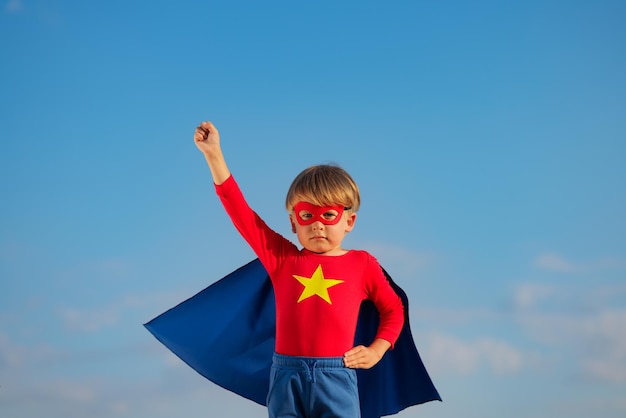 Superhero child playing outdoor super hero kid against blue
summer sky background imagination and freedom concept