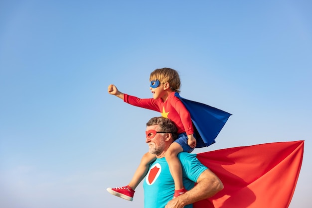 Superhero senior man and child playing outdoor super hero\
grandfather and boy having fun together against blue summer sky\
background family holiday concept happy fathers day