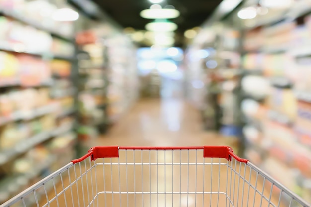 Supermarket aisle and product shelves background with empty shopping cart