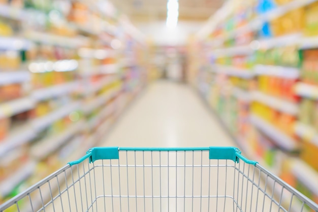 Supermarket aisle with empty shopping cart and product shelves interior defocused blur background