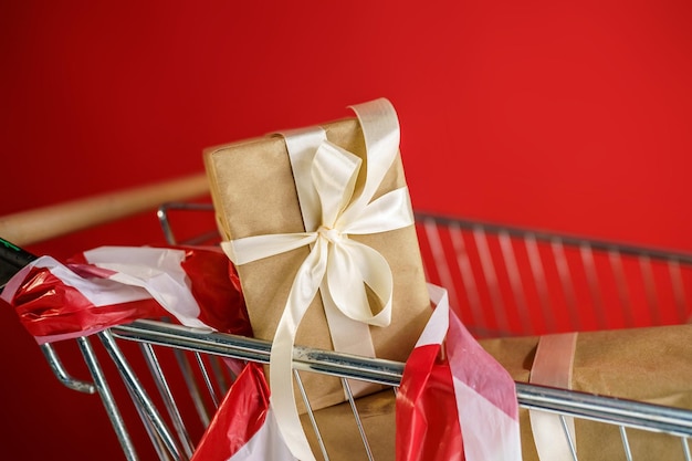 Supermarket basket with gifts wrapped in craft paper with a white ribbon on a red background