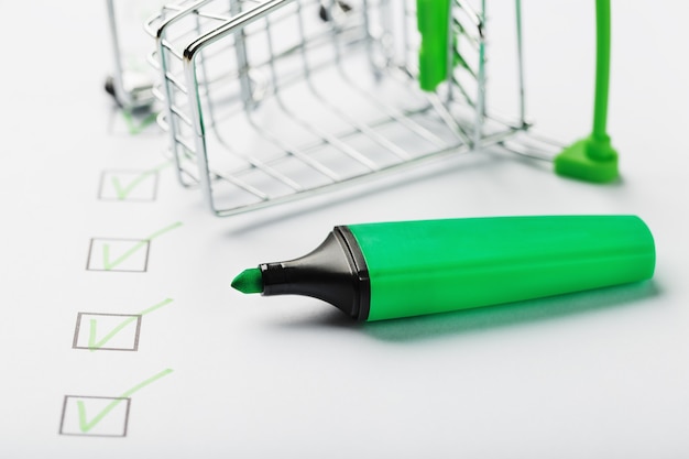 Фото Тележка супермаркета и зеленый маркер отмечены на листе контрольного списка. контрольный список покупок завершил концепцию задачи.
