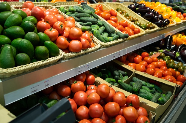 Supermarket counter with wicker baskets and lug boxes with tomatoes, cucumbers and avocados