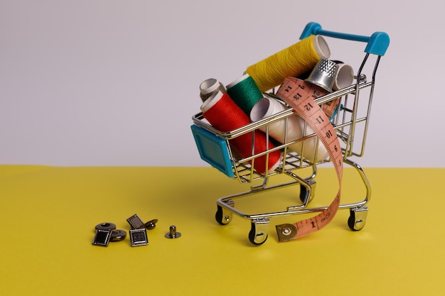 supermarket trolley with colored sewing threads on a white-yellow background