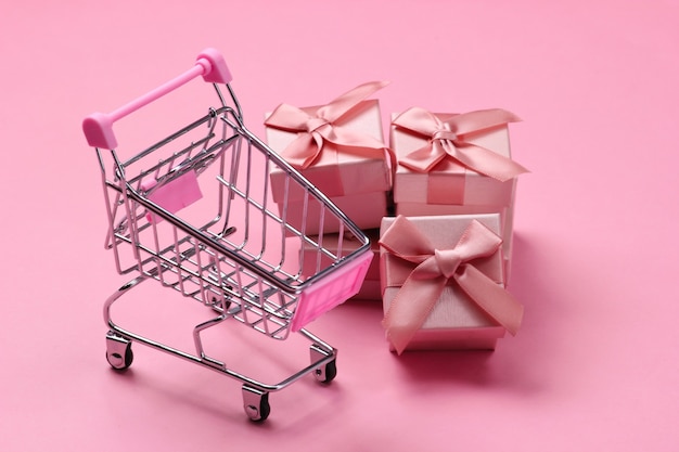 Carrello del supermercato con scatole regalo su pastello rosa