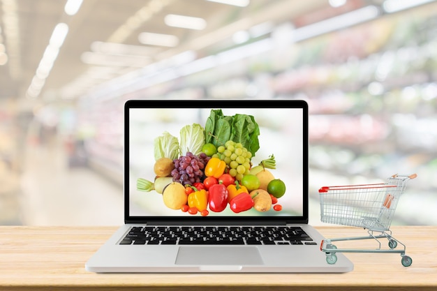 Supermarkt gangpad wazig achtergrond met laptopcomputer en winkelwagentje op houten tafel kruidenier online concept