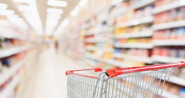 Supermarkt gangpad wazig achtergrond met lege rode winkelwagen