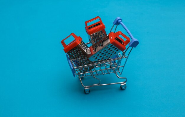 Supermarktkarretje met miniraspen op blauwe achtergrond.