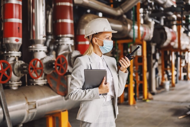 Supervisor holding tablet and talking over walkie talkie while standing in plant