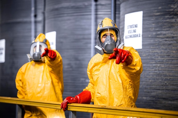 supervisor in beschermingsmiddelen en gasmasker die het proces van chemische productie uitlegt aan stagiair