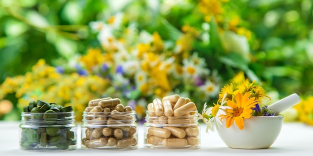 흐릿한 꽃 배경이 있는 흰색 탁자에 있는 유리병에 든 보충제와 비타민