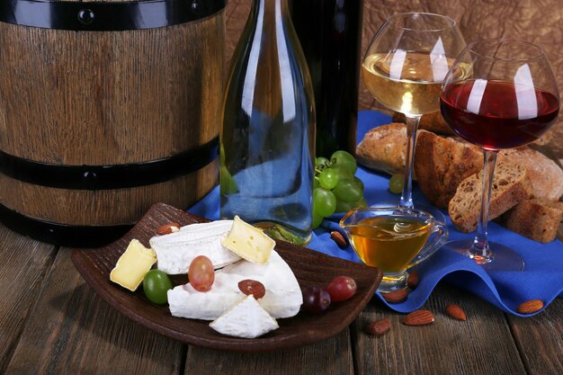 Supper consisting of Camembert and Brie cheese honey wine and grapes on napkin in basket and wine barrel on wooden table on brown background