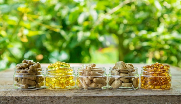 Supplementen, vitamines en geneeskrachtige kruiden in glazen potten op houten tafel op wazige plantenachtergrond