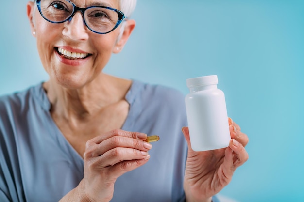 Supplements Senior woman holding capsule and a blank white supplement container