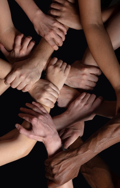 Support. Hands of people's crows in touch isolated on black studio background. Concept of human relation, community, togetherness, symbolism. Hard and strong touching, creating one unit.