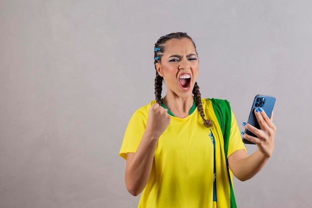 Supporter of the Brazilian football team celebrating a goal by watching the smartphone