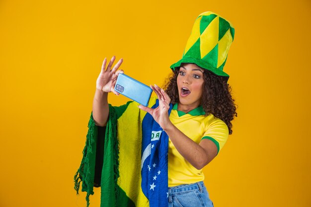 Photo supporter of the brazilian football team celebrating a goal by watching the smartphone