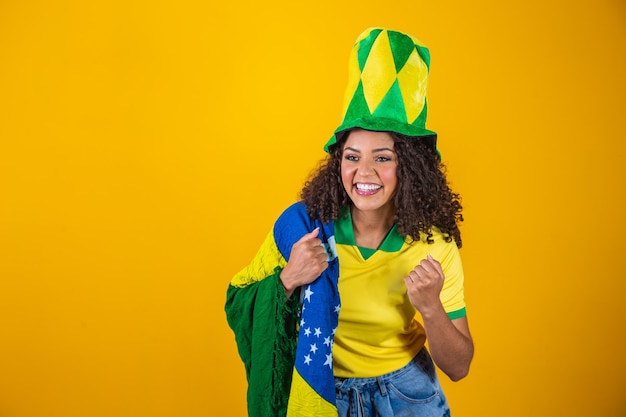 Supporter van Brazilië. Braziliaanse krullend haar vrouw fan vieren op voetbal, voetbalwedstrijd op gele achtergrond. Brazilië kleuren.