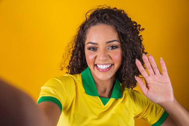 Supporter van Brazilië. Braziliaanse vrouw fan vieren op voetbal, voetbalwedstrijd op gele achtergrond. Brazilië kleuren. Selfie-smartphone.