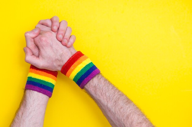 Supporting hands with gay pride rainbow flag wristband on a yellow background