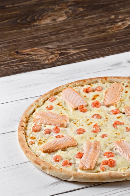 Foto la pizza suprema con salmone e gamberi è servita sul tavolo di legno. pizza ai frutti di mare