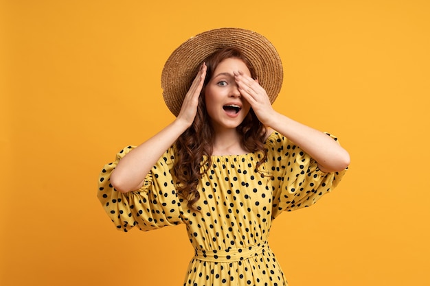 Suprice face. portrait of red head woman in straw hat posing on yellow in summer dress.