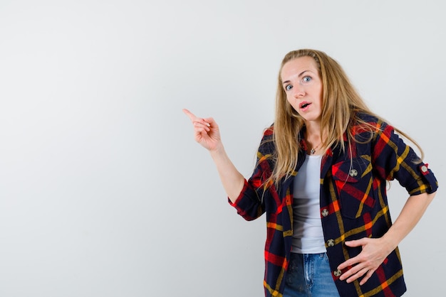 The suprised woman is poinintg to left with her forefinger on white background