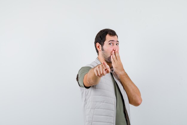 The suprised  young man is pointing to camera with forefinger on white background