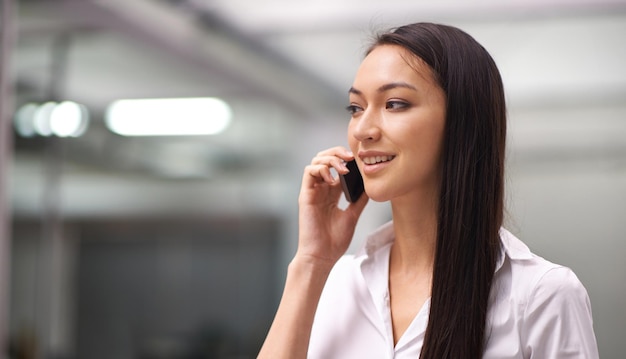 確かに私たちはあなたのためにそれをすることができますオフィスで彼女の携帯電話を使用している魅力的な若い女性のトリミングされたショット