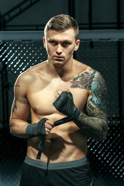 Sure you can handle him? Vertical portrait of a handsome professional male boxer wrapping hands bandages looking away seriously