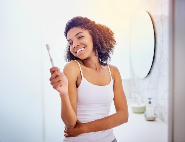 Самый верный способ хорошо провести день Снимок привлекательной молодой женщины, чистящей зубы в ванной дома