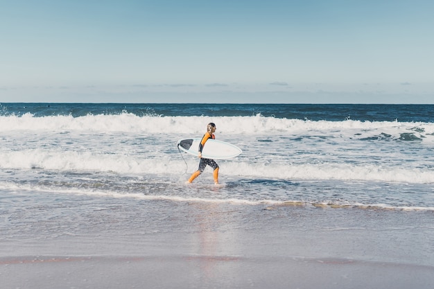 surf girl on the ocean coast in a wet suit with surf board