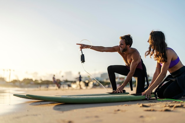 A surf instructor is pointing at good wave while a girl smiling and watching