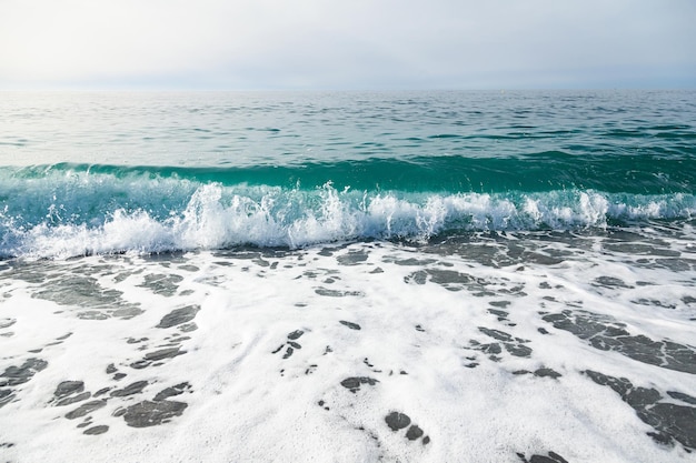 Surf of the sea wave with clear water on the coast with small stones