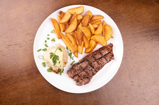 Surf and turf fried fish dish with grilled steak and potatoes top view over wooden table