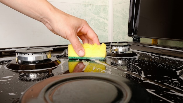 Foto pulizia delle superfici, stufa a gas di lavaggio della donna con un panno giallo e un detersivo.