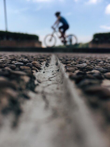 Photo surface level of pebbles on road with man cycling in background