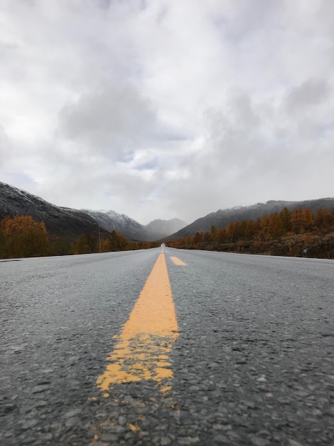 Foto immagine a livello di superficie della strada che conduce verso la montagna contro un cielo nuvoloso