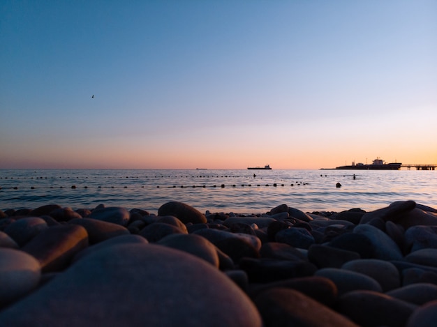 Surface level of stones on beach against sunset on sea. Stone Black sea shore. Waves, splashes, water surface texture. Picturesque panoramic scenery, copy space, graphic resources