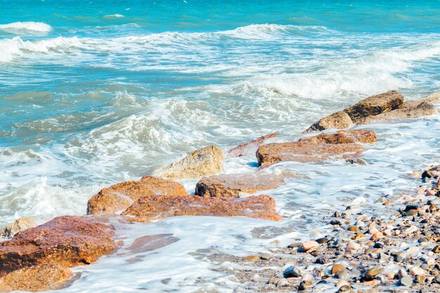 Photo surface of sea waves during windy summer day sea shore with pebble stones and cutwater