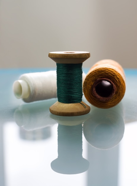 The surface of the table creates a reflection of three spools with colored threads