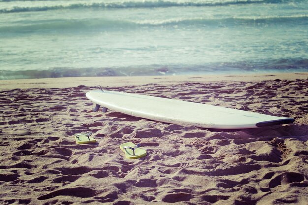 Photo surfboard and flip flops on the sand in vintage tone