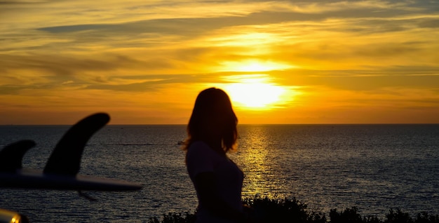 Surfboard and girl by the sea at sunset