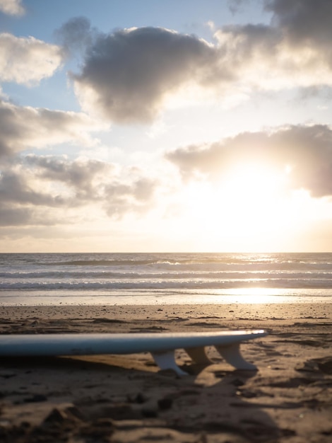 Photo a surfboard lying on the beach at sunrise