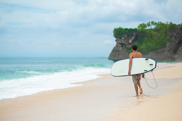 Foto surfen man met surfplank lopen op tropisch zandstrand. gezonde levensstijl, wateractiviteiten