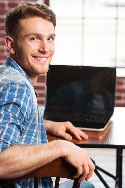 Surfen op het net is leuk. Achteraanzicht van een knappe jongeman die over zijn schouder kijkt en glimlacht terwijl hij op zijn werkplek zit