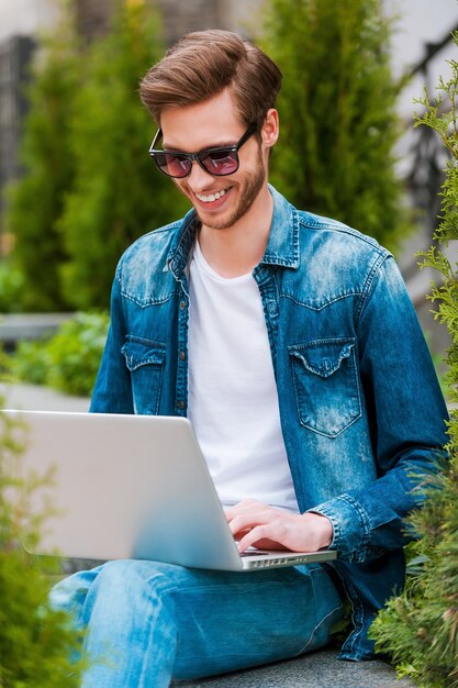 Surfen op het web buitenshuis. glimlachende jonge man die op laptop werkt terwijl hij buiten zit